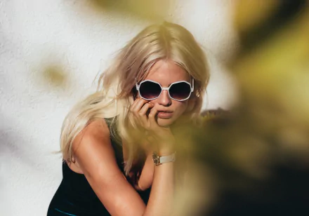 HD desktop wallpaper featuring fashion model Becca Hiller with blonde hair, wearing sunglasses and a black outfit, set against a blurred background.