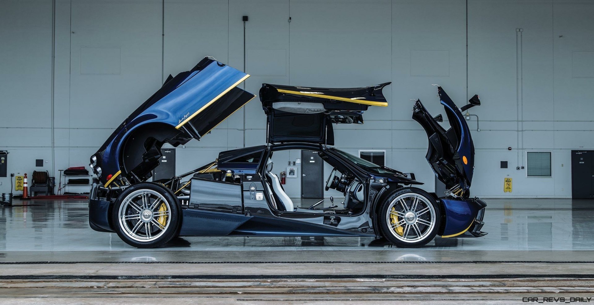 A sleek Pagani Huayra supercar with open doors and panels, showcased in a clean, industrial garage setting as a high-definition PC desktop wallpaper.