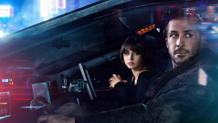 HD desktop wallpaper featuring Ana de Armas as Joi and Ryan Gosling as Officer K from the movie Blade Runner 2049. The two characters are sitting in a futuristic car with neon city lights in the background.