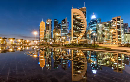 HD desktop wallpaper of Doha, Qatar at night, showcasing illuminated skyscrapers and their reflections in water, capturing the city's modern architecture and vibrant atmosphere.