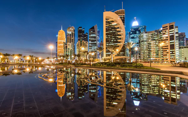 HD desktop wallpaper of Doha, Qatar at night, showcasing illuminated skyscrapers and their reflections in water, capturing the city's modern architecture and vibrant atmosphere.
