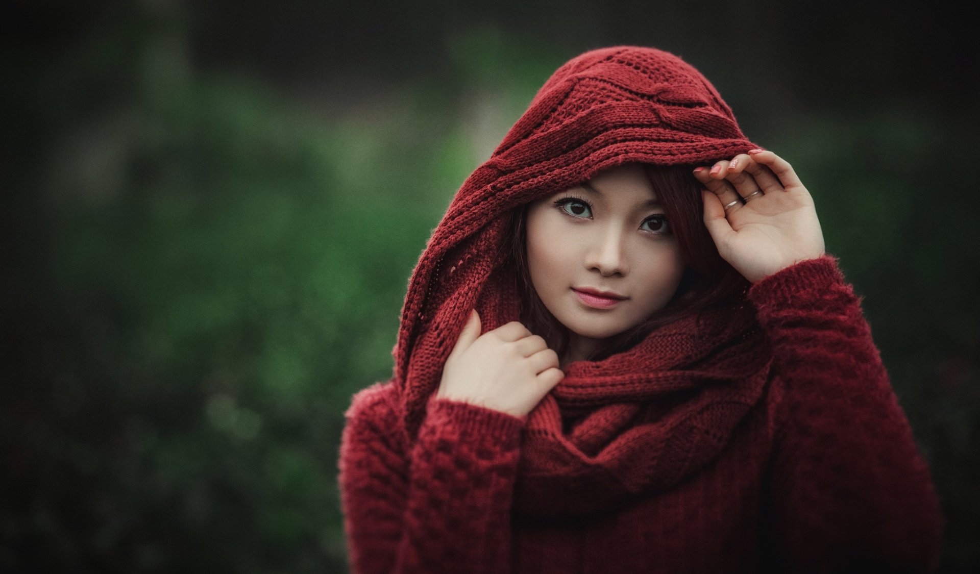 A high-definition desktop wallpaper featuring an Asian model with brown eyes and a red scarf, captured with a depth-of-field effect, highlighting her serene expression against a blurred green background.