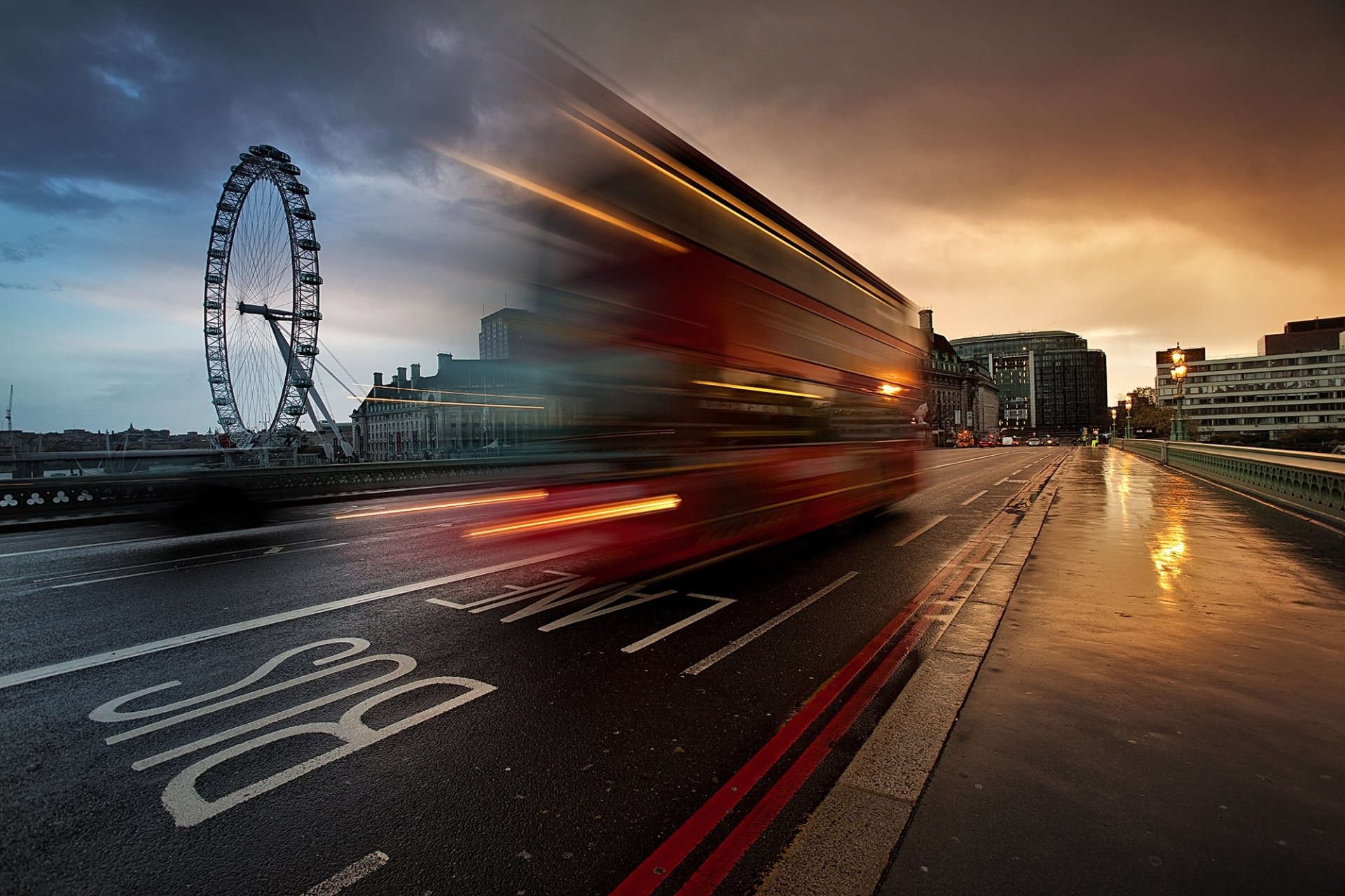 London’s iconic Ferris wheel with a red double-decker bus captured in motion blur on a wet street at dusk, creating a dynamic HD desktop wallpaper scene.