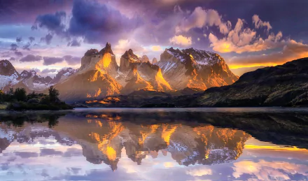Sunlit peaks of Torres del Paine in the Chilean Andes reflect vividly on a calm lake, showcasing the stunning natural beauty of Patagonia at sunrise.