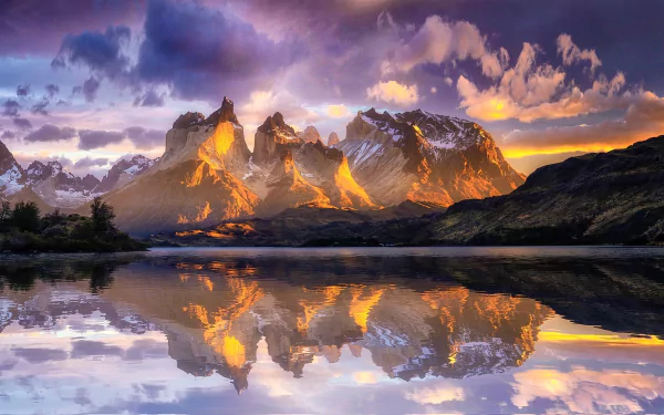 Sunlit peaks of Torres del Paine in the Chilean Andes reflect vividly on a calm lake, showcasing the stunning natural beauty of Patagonia at sunrise.