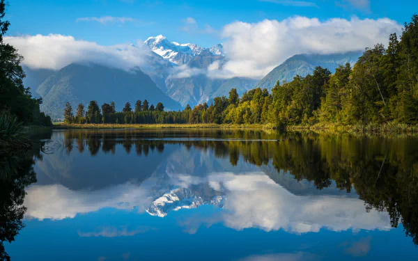 HD desktop wallpaper showing Aoraki/Mount Cook reflected in Lake Matheson with clouds and lush greenery in New Zealand's natural landscape.