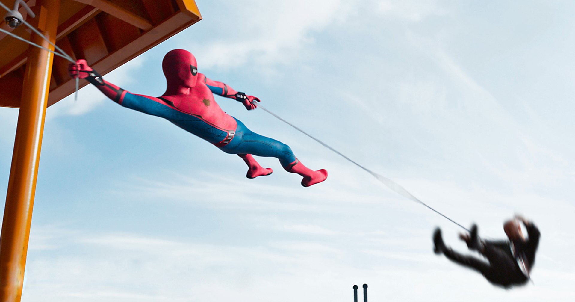 Spider-Man swinging on a web in an action scene from the movie Spider-Man: Homecoming, set against a clear blue sky. HD desktop wallpaper and background.