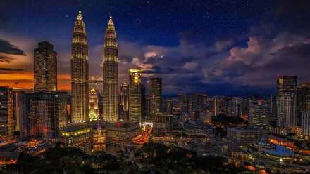 Night cityscape of Kuala Lumpur, Malaysia, featuring illuminated Petronas Towers skyscrapers and surrounding man-made buildings, glowing lights against a starry sky — HD desktop wallpaper.
