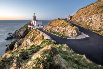 Baily Lighthouse on a cliff in Ireland at sunrise, morning sea and horizon, a winding coastal road leading to the man-made lighthouse — HD desktop wallpaper.