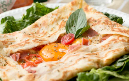 HD desktop wallpaper featuring a pita sandwich filled with a sunny-side-up egg, cherry tomatoes, and fresh herbs on a bed of leafy greens.