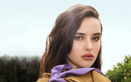 Brunette Australian actress Katherine Langford poses with a soft expression, featuring a stylish outfit and a faint natural background, captured in high-definition detail.