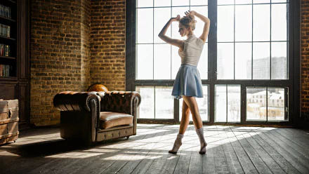Blonde woman in a skirt dancing gracefully near large industrial windows, captured in a mood-filled, high-definition desktop wallpaper setting.