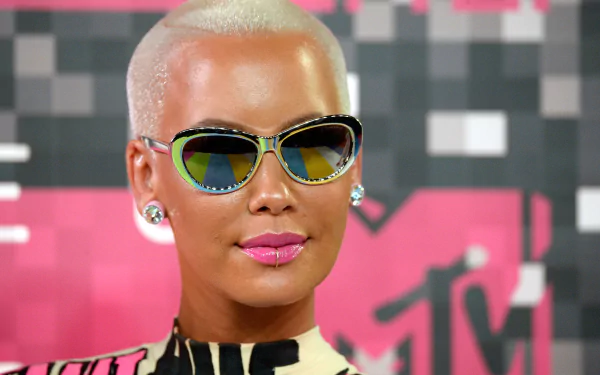 HD desktop wallpaper featuring a person with blonde buzz cut and reflective sunglasses against a pink graphic background.