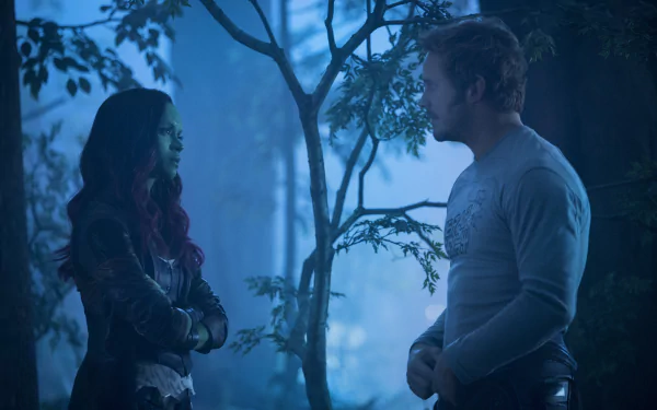 Star-Lord and Gamora stand facing each other in a blue-lit forest scene from Guardians of the Galaxy Vol. 2 — 5K Ultra HD PC desktop wallpaper.