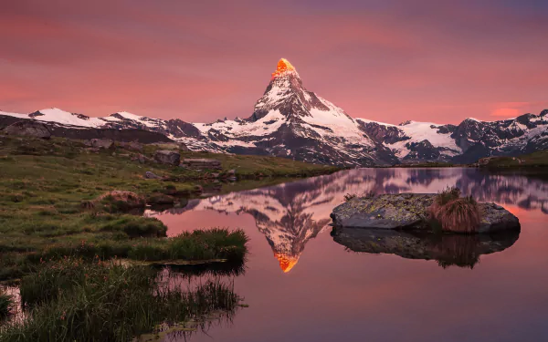 HD desktop wallpaper showcasing the Matterhorn mountain peak reflected vividly in a calm lake at sunset, surrounded by lush greenery and a serene natural landscape.
