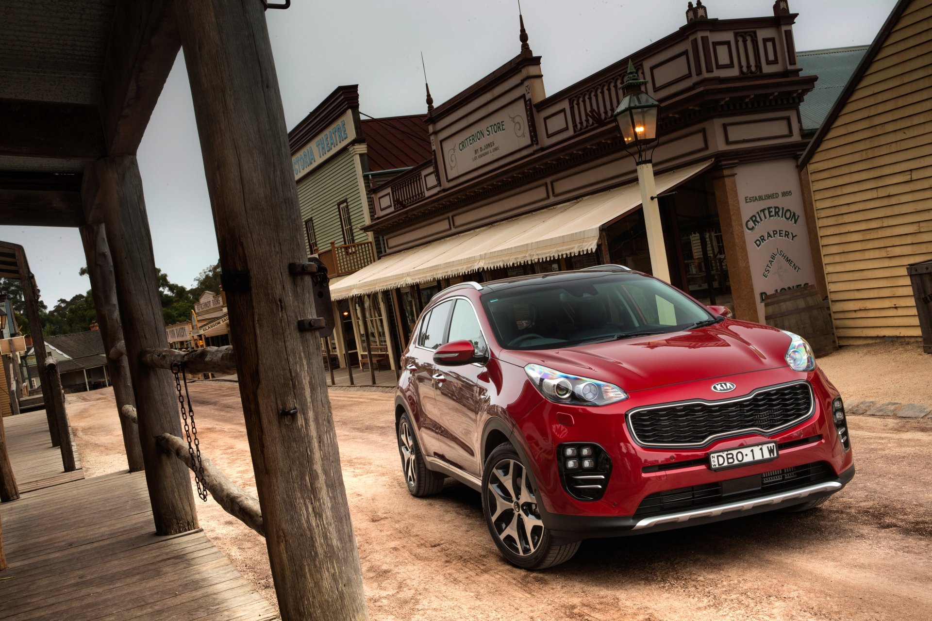 Red Kia Sportage SUV parked on a dusty Old West main street — 4K Ultra HD PC desktop wallpaper and background showcasing the Kia vehicle.