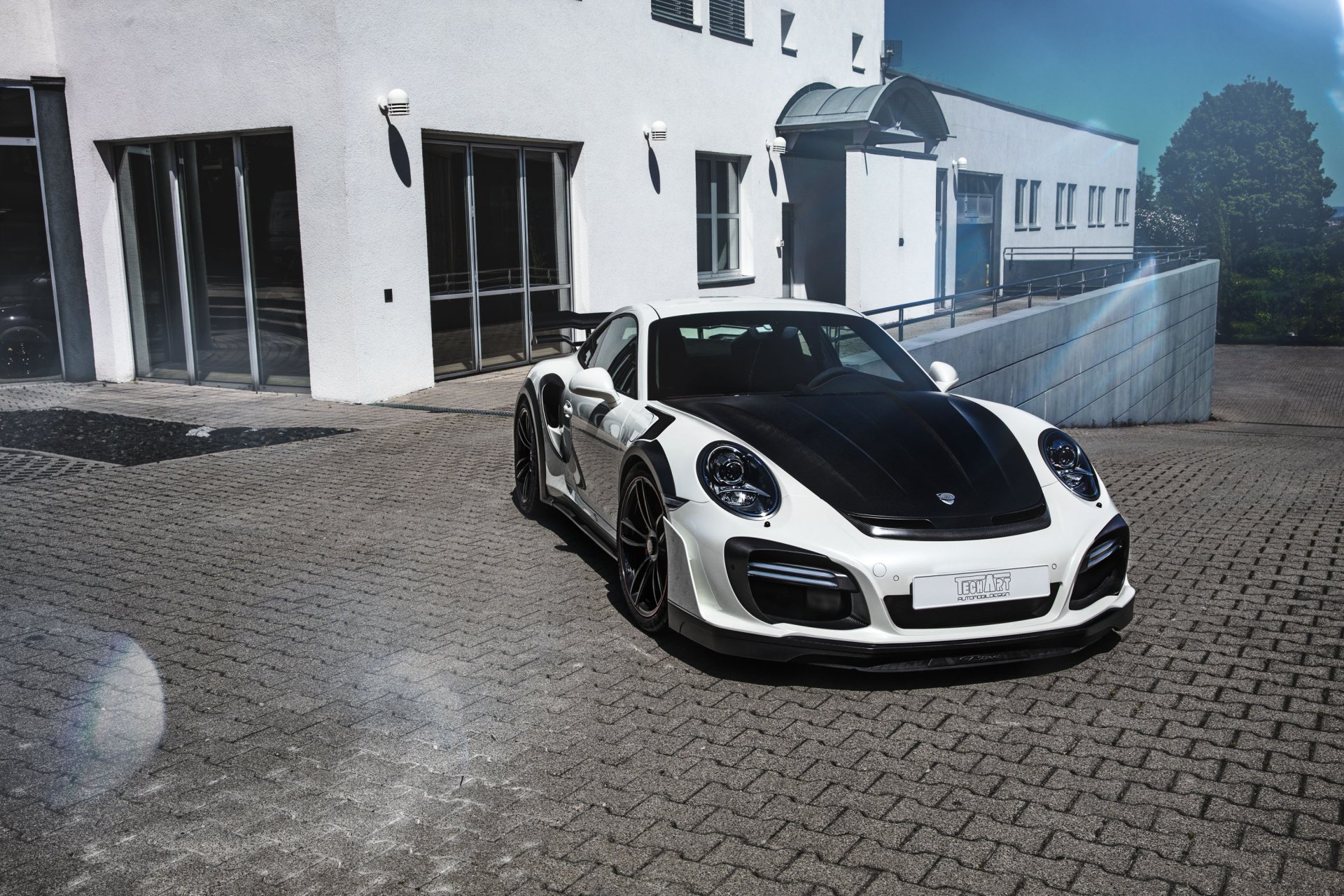 2K Quad HD PC wallpaper of a white Porsche 911 Turbo sports car parked by a modern building, front three-quarter view of the vehicle.