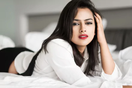 HD desktop wallpaper of an Indian woman with long dark hair and red lipstick reclining on a bed, looking at the camera in a white blouse.
