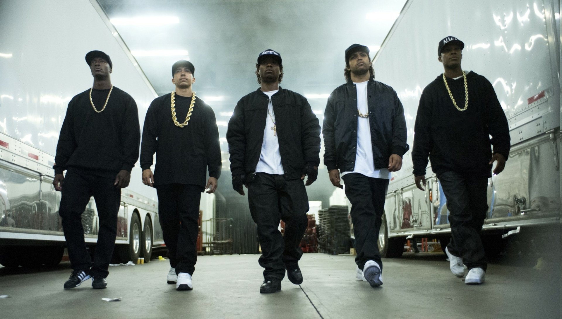 Five members of N.W.A. walk confidently down a dimly lit corridor, dressed in black with gold chains, embodying the spirit of hip-hop culture in this HD music wallpaper.
