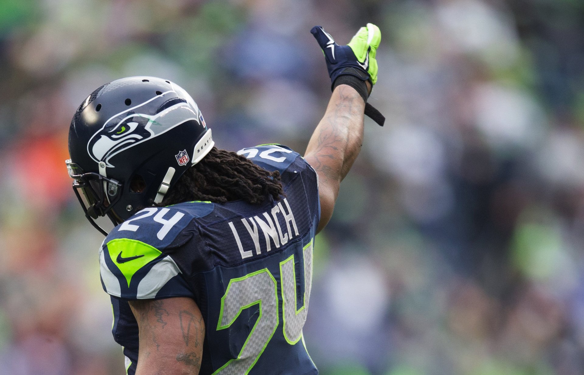 HD wallpaper featuring Seattle Seahawks player Marshawn Lynch #24 on the field, in full uniform, raising his hand to the crowd.