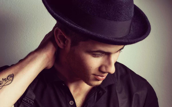 HD desktop wallpaper featuring a person in a black shirt and hat, glancing downward with a thoughtful expression.