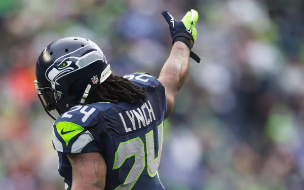HD wallpaper featuring Seattle Seahawks player Marshawn Lynch #24 on the field, in full uniform, raising his hand to the crowd.