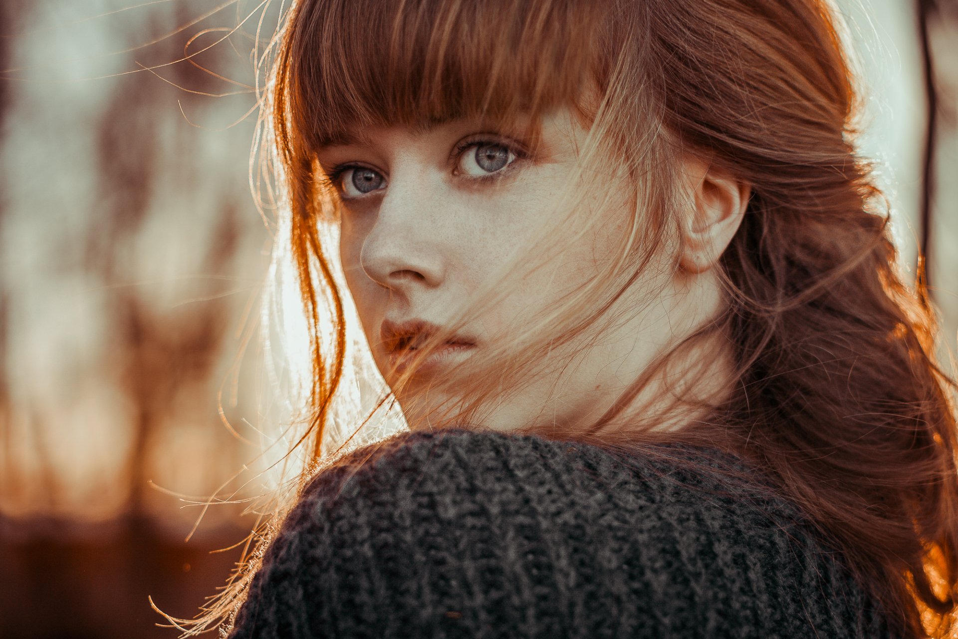 HD desktop wallpaper featuring a redhead woman with blue eyes, posing outdoors with a soft depth of field.