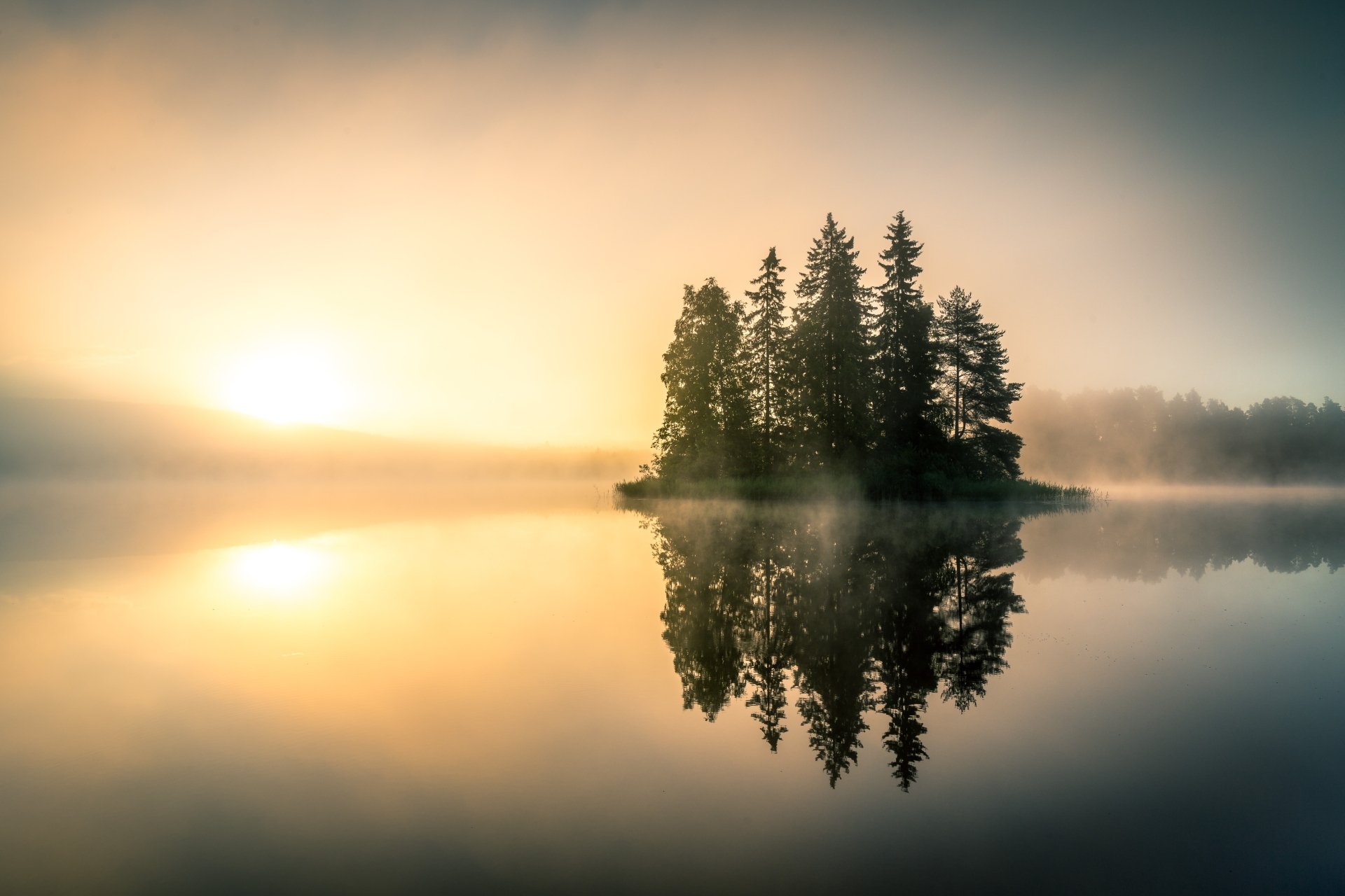 HD desktop wallpaper of a serene lake at sunrise, enveloped in fog. Trees on a small island are reflected perfectly in the still water.