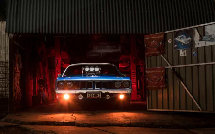 HD desktop wallpaper of a blue Plymouth Barracuda muscle car by Chrysler, illuminated in a dark garage with red lighting.
