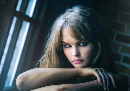 HD desktop wallpaper featuring a portrait of blonde, blue-eyed Russian model, Anastasiya Scheglova, gazing intently at the camera with her arms resting on a windowsill.