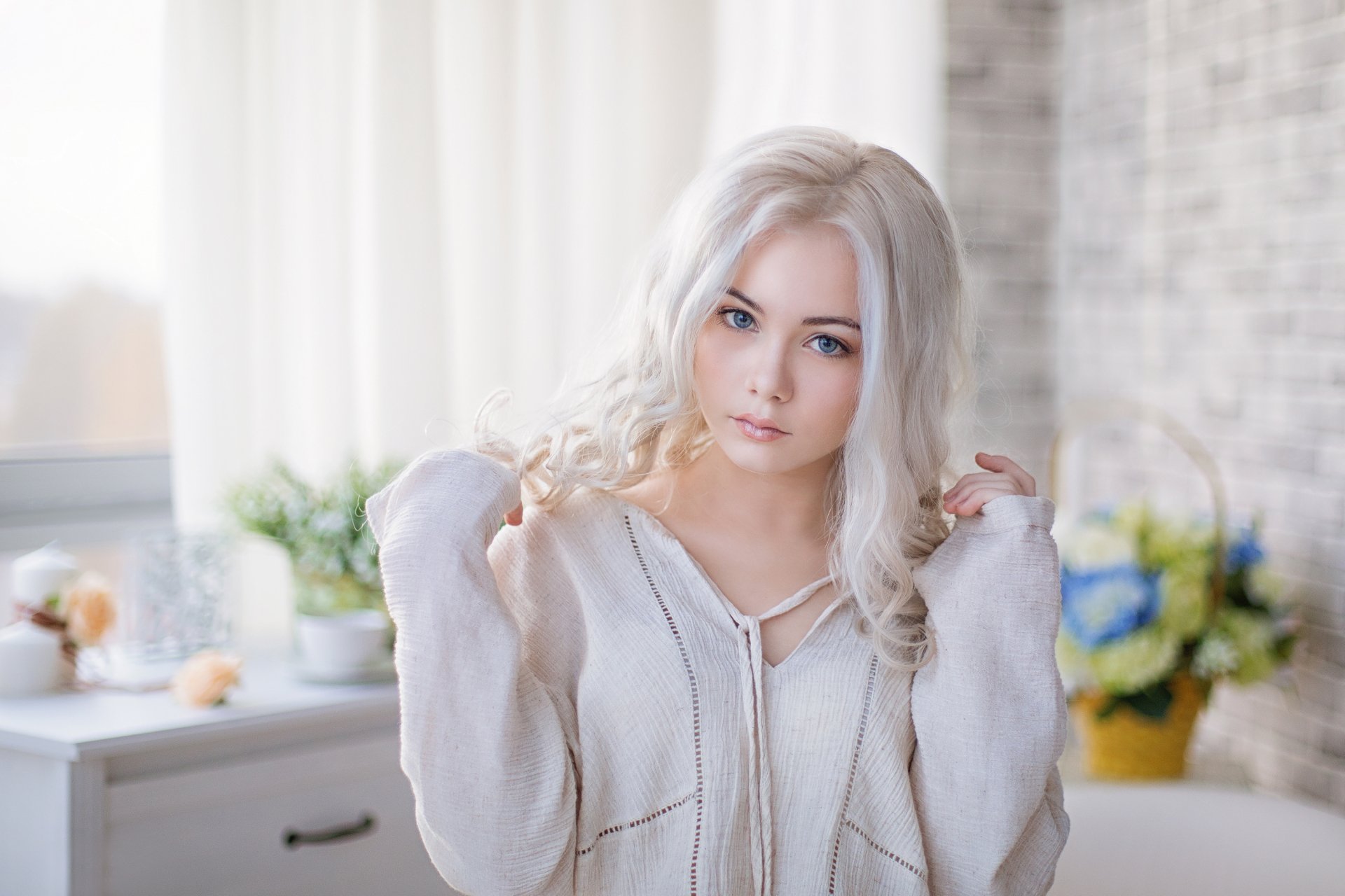 HD desktop wallpaper featuring a model with white hair and blue eyes, captured with a depth of field effect. She stands in a softly lit room with blurred background elements.