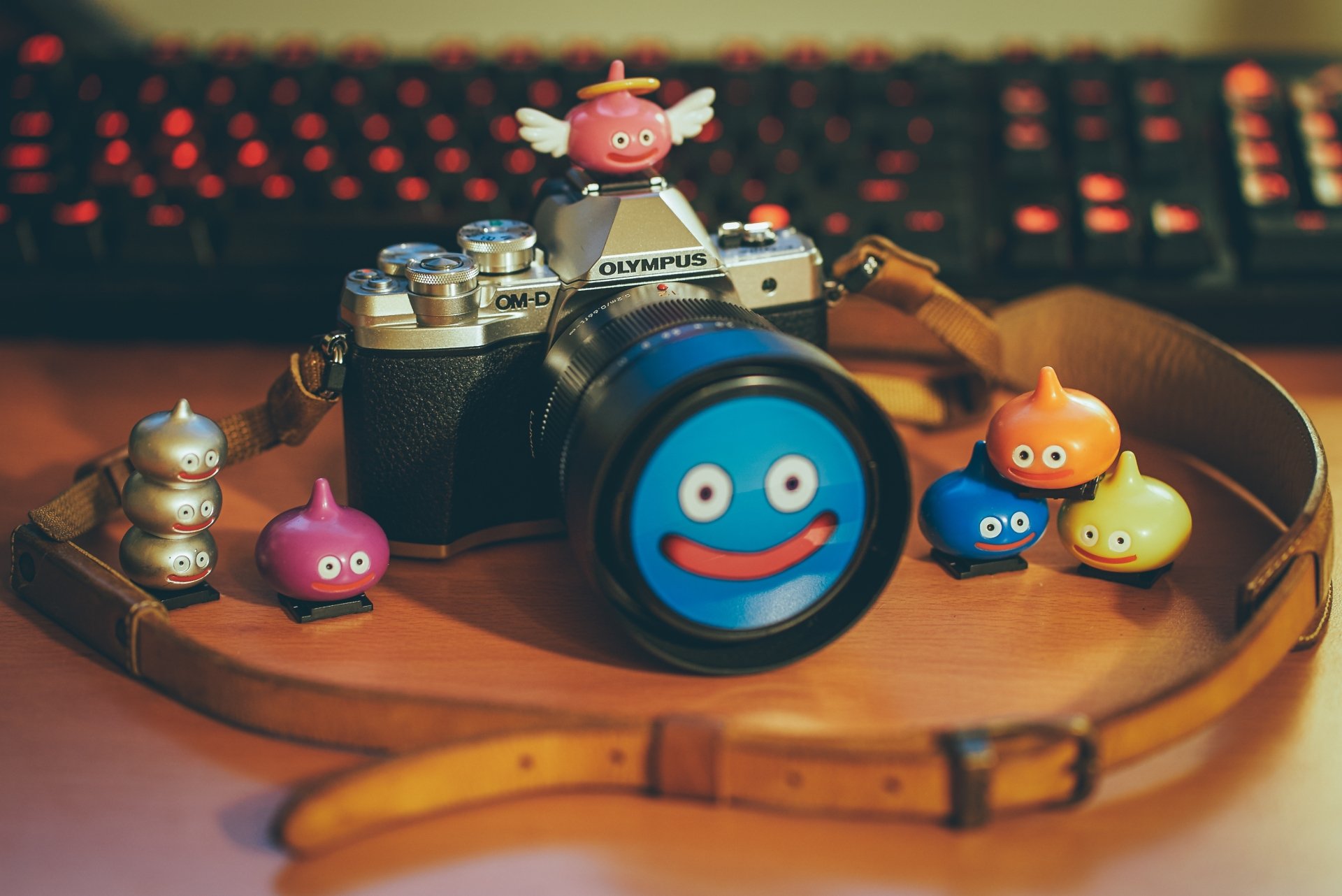 A 4K Ultra HD image of a man-made Olympus camera with a close-up lens, surrounded by colorful Dragon Quest Slime figurines on a wooden surface.