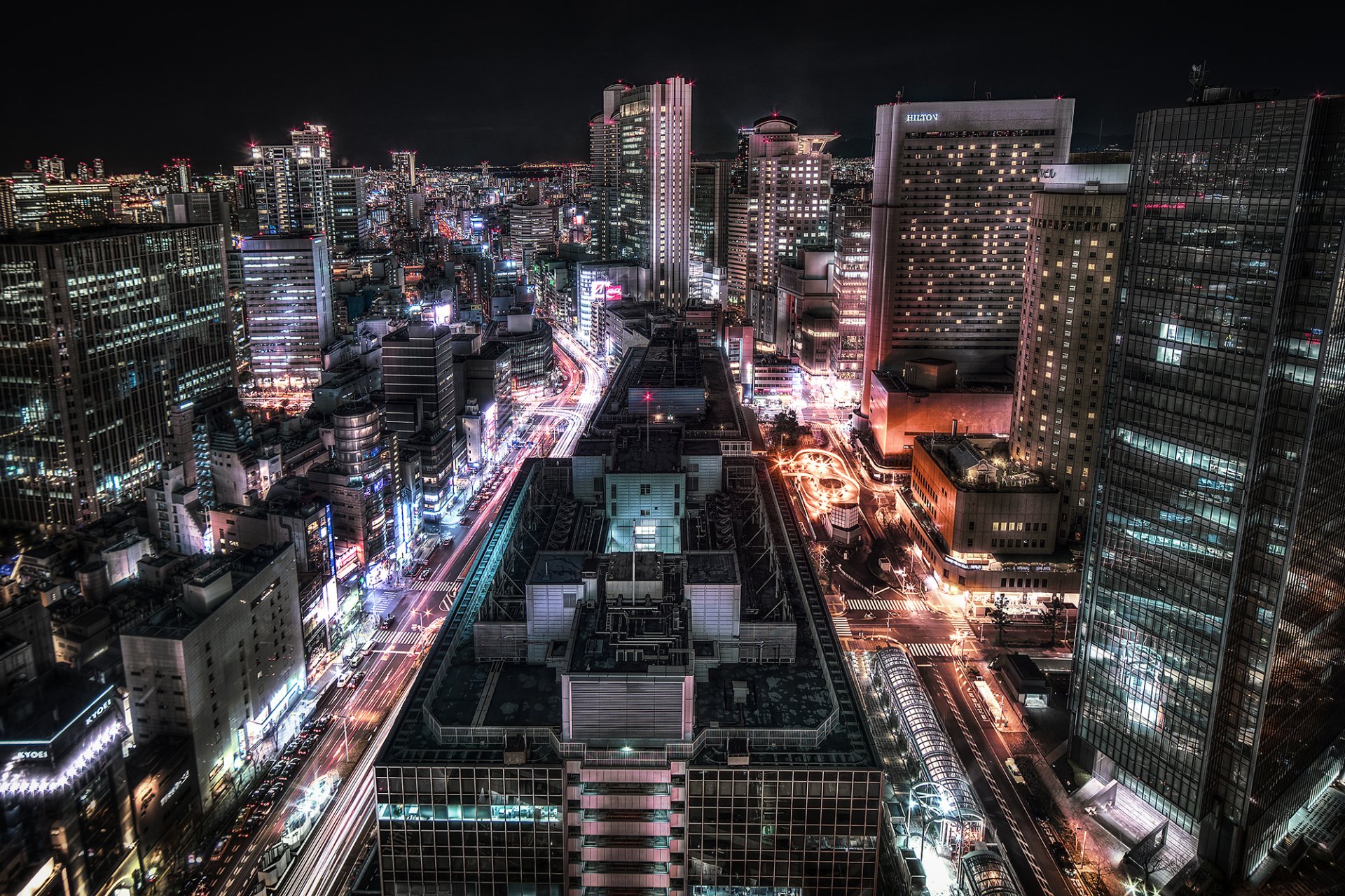 HD PC desktop wallpaper of Osaka at night: illuminated skyscrapers and roads weaving through a dense, man-made urban skyline in Japan.