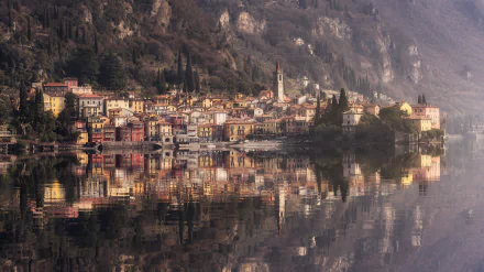HD desktop wallpaper of Varenna, an Italian village by a lake, showcasing colorful houses and their reflection on the calm water beneath rocky cliffs.