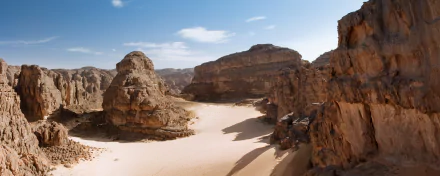 High-definition wallpaper of Tassili N'Ajjer National Park in Algeria, showcasing the Sahara desert's sandy landscape and rugged rock formations under a bright blue sky.