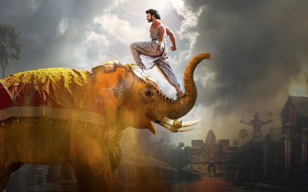 An HD desktop wallpaper depicting a scene from Baahubali 2: The Conclusion, featuring a man standing atop a decorated elephant against a dramatic, cloudy background.