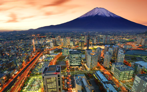 HD desktop wallpaper featuring a stunning cityscape of Yokohama, Japan. Skyscrapers illuminate the bustling city with majestic Mount Fuji standing proudly in the background against a vibrant sunset sky.