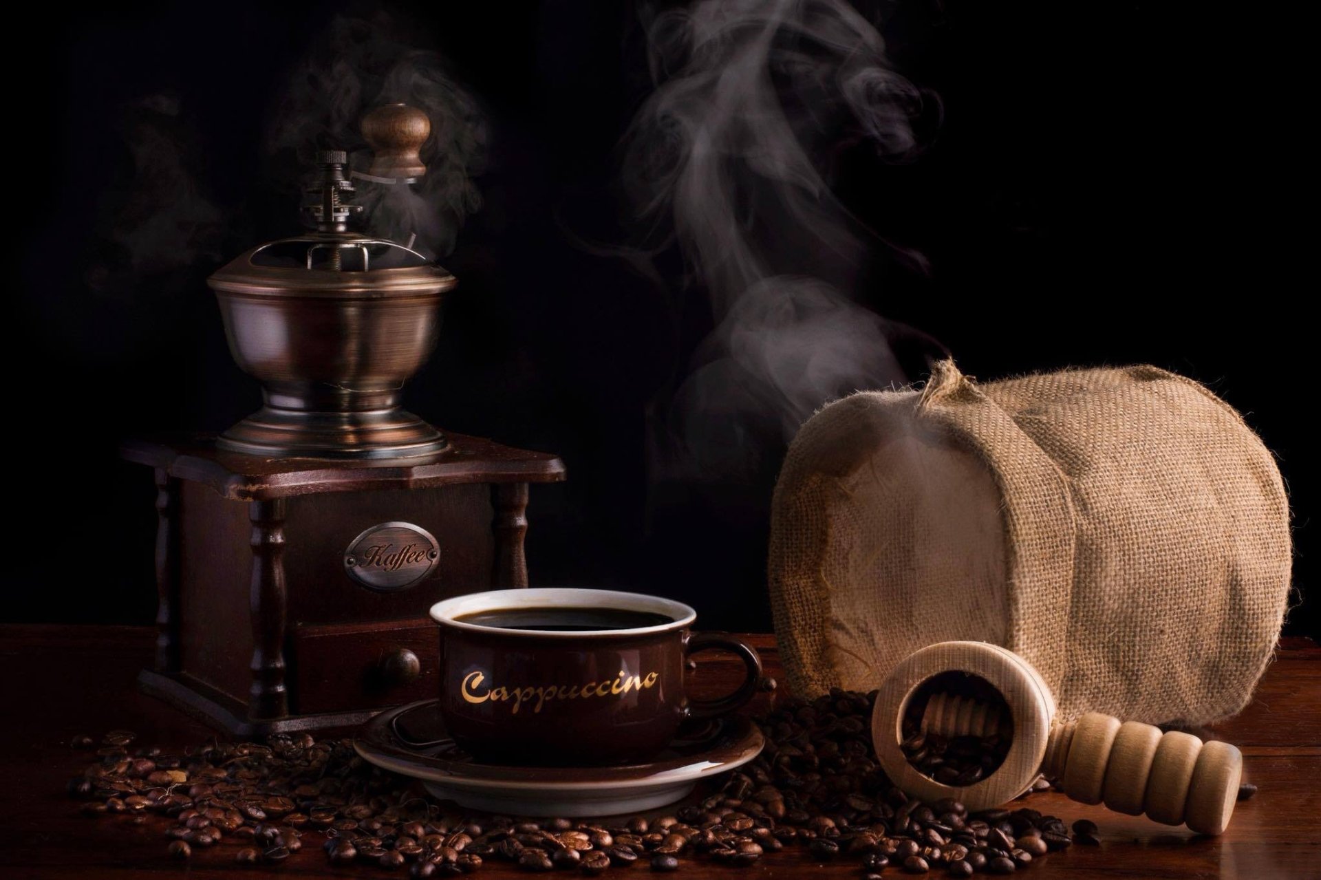 HD PC desktop wallpaper still life of coffee: vintage grinder, steaming cup, burlap sack and scattered coffee beans on a dark background.