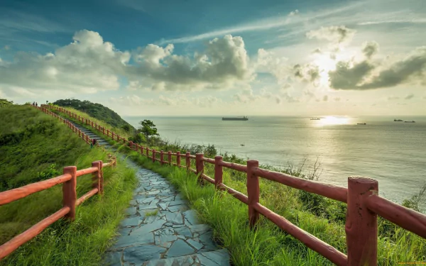 Serene HD wallpaper of a coastline path with a stone walkway and a wooden fence, overlooking the sea and horizon on a sunny day.