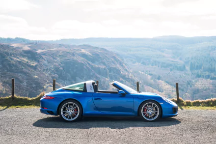 Blue Porsche 911 Targa 4S parked on a roadside with scenic mountainous landscape in the background. 4K Ultra HD PC desktop wallpaper and background.