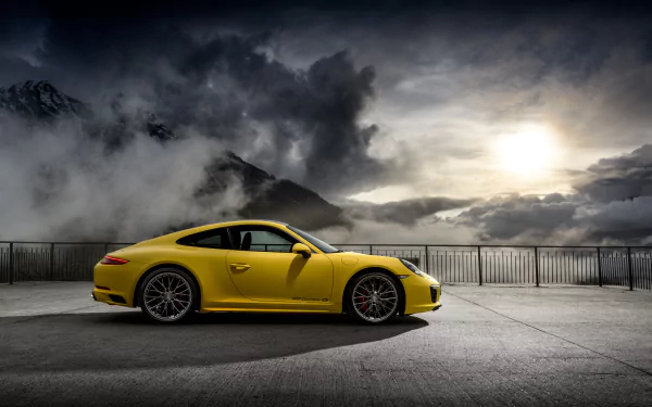 Yellow Porsche 911 Carrera 4S parked on a mountain overlook with dramatic cloudy sky, captured in stunning 4K Ultra HD for a PC desktop wallpaper.