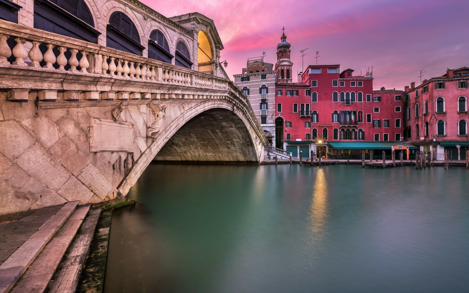 2K Quad HD desktop wallpaper: Venetian Rialto Bridge spanning a calm canal with colorful houses along the water at sunset, man-made stone bridge in Italy.