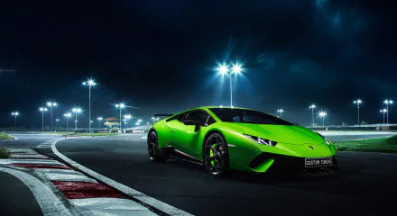 A vibrant green Lamborghini Huracan Performante supercar is parked on a race track at night, illuminated by bright overhead lights in this HD desktop wallpaper.
