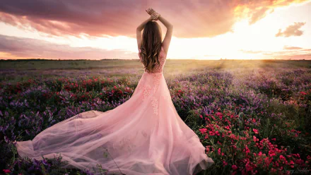 A woman in a flowing pink dress stands with her back to the camera in a vibrant flower field at sunset, creating a serene and dreamy mood in this HD desktop wallpaper.