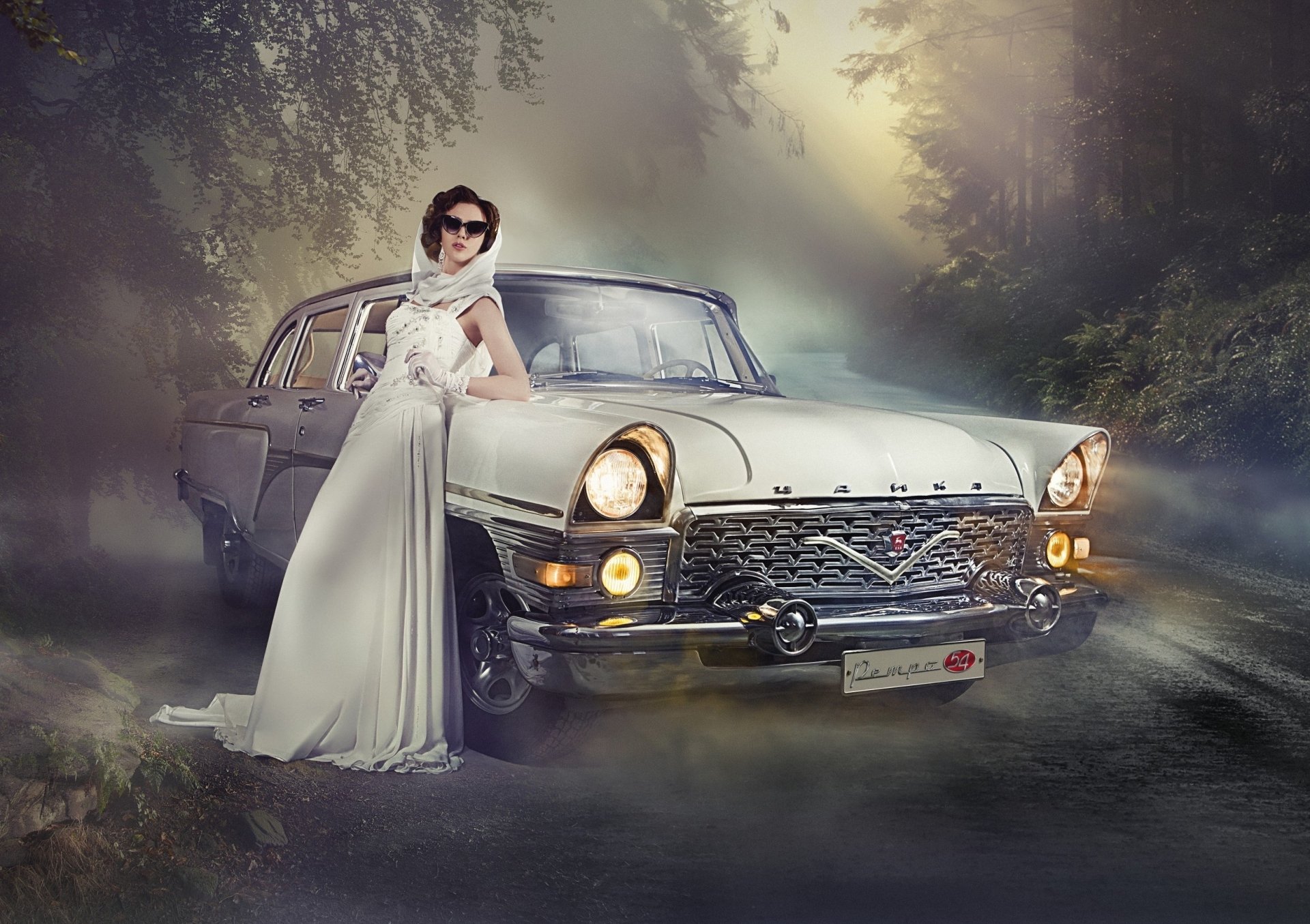 A fashionable woman in a white gown poses confidently beside a vintage car on a misty road, capturing a stylish blend of elegance and classic automotive design for an HD desktop wallpaper.