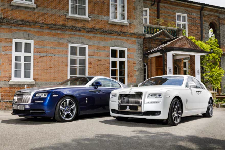 A stunning HD desktop wallpaper featuring two elegant Rolls-Royce cars, a blue Wraith and a white Ghost, parked in front of a brick mansion.