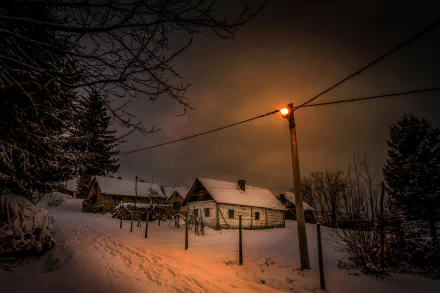 Snow-covered houses and trees are softly illuminated by a glowing street light on a serene winter night, captured in this HD desktop wallpaper.