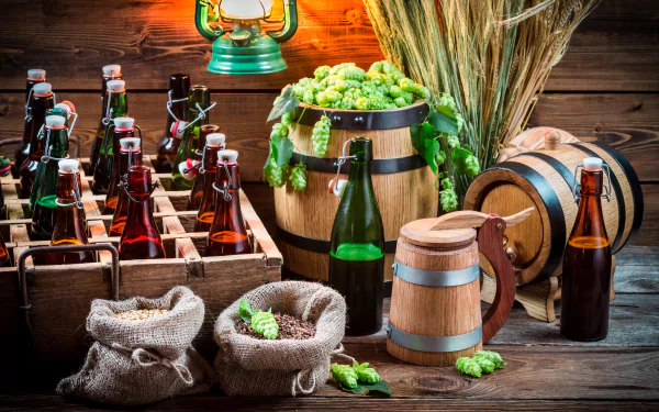 HD desktop wallpaper of a still life setup featuring bottles of beer, barrels, hops, and ingredients on a rustic wooden background.