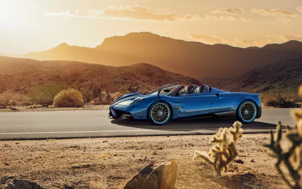 A blue Pagani Huayra Roadster supercar parked on a desert road with mountains in the background, captured in 4K Ultra HD as a PC desktop wallpaper.