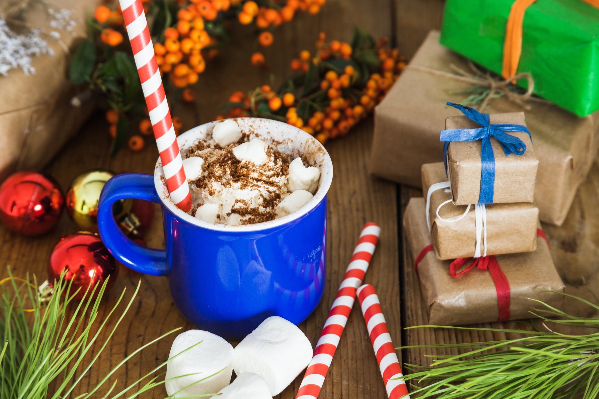 A vibrant still life 4K Ultra HD wallpaper featuring a blue cup of hot chocolate with marshmallows and candy canes, surrounded by wrapped gifts and festive decorations.